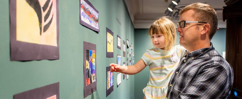 man holding little girl as they look at the artwork on the walls